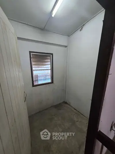 Compact storage room with window and concrete floor, ideal for organizing household items.