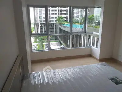 Spacious bedroom with large windows offering a stunning view of modern apartment complex and pool.