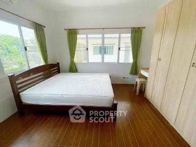 Spacious bedroom with large windows and wooden flooring in a serene setting.