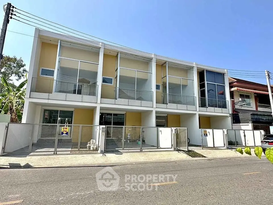 Modern townhouse exterior with large windows and gated entrance on a sunny day.