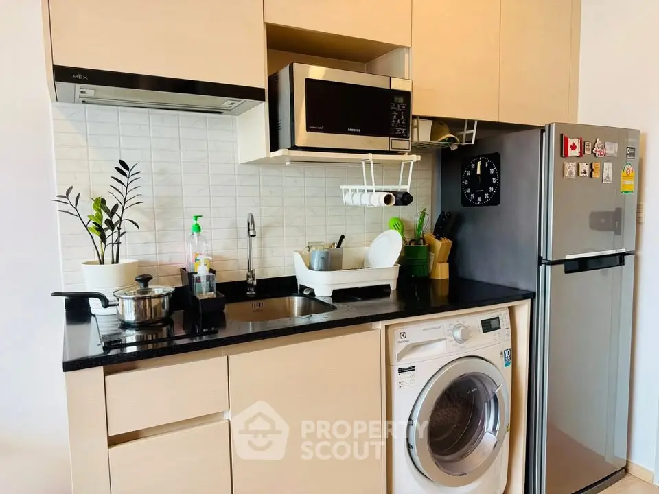 Modern kitchen with washing machine, microwave, and sleek cabinetry in compact layout.