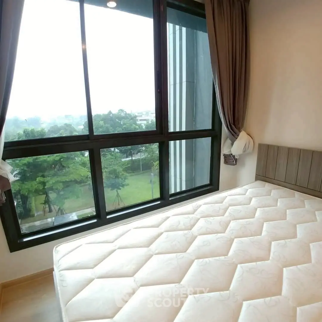 Bright bedroom with large window offering scenic garden view in modern apartment.
