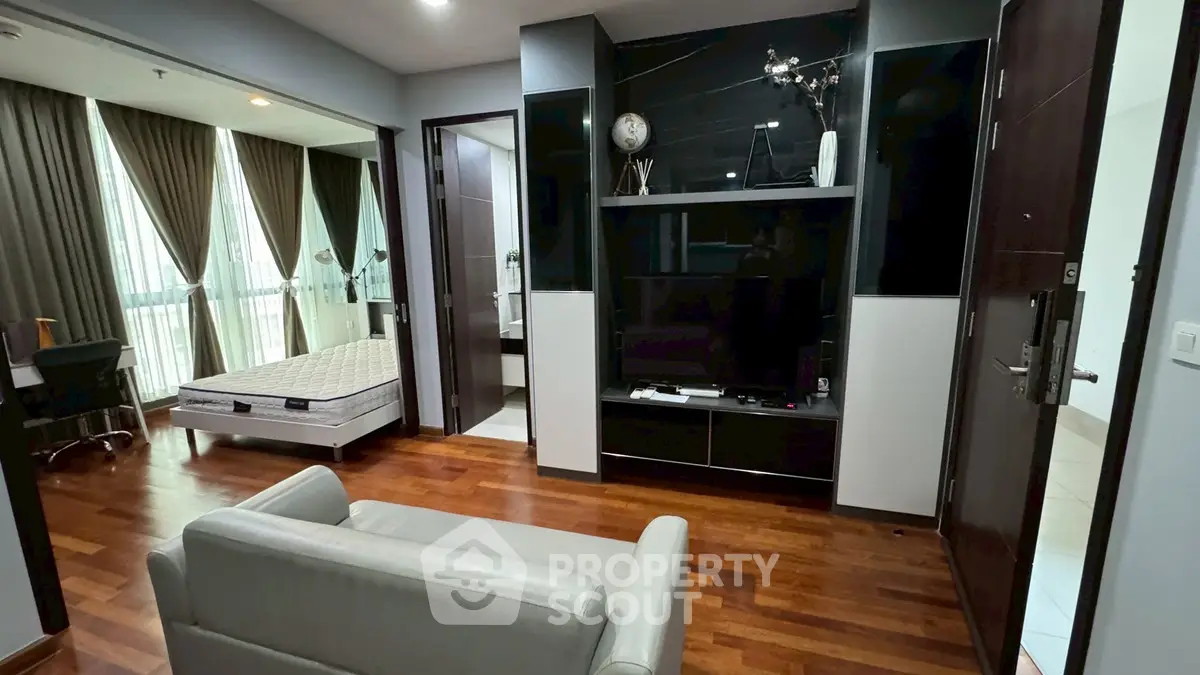 Modern apartment interior with hardwood floors, featuring a cozy living area and a glimpse of the bedroom.