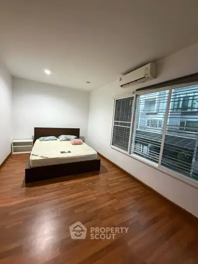 Spacious bedroom with wooden flooring and large window in modern apartment