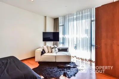 Modern bedroom with sleek design and natural light, featuring a cozy sofa and wall-mounted TV.