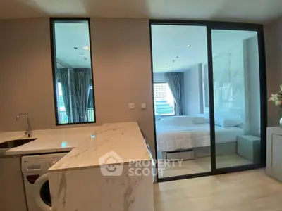 Modern apartment with open kitchen and cozy bedroom, featuring sleek marble countertops and large windows.