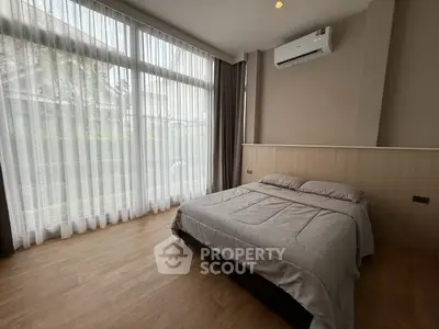 Spacious bedroom with large windows and modern decor, featuring an air conditioner and elegant curtains.