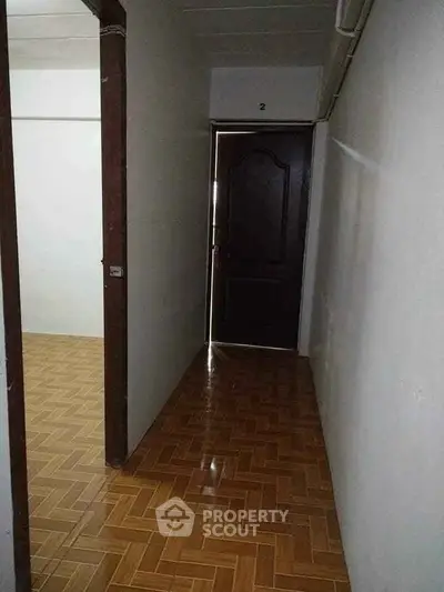 Narrow hallway with wooden flooring leading to a dark wooden door in a residential property.