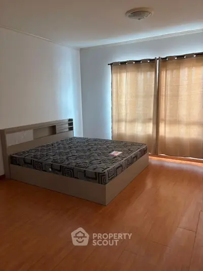 Spacious bedroom with wooden flooring and large windows for natural light.