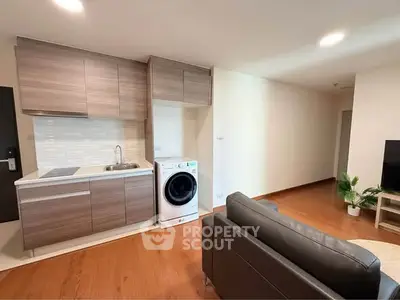 Modern apartment interior with compact kitchen and cozy living area, featuring wooden flooring and a washing machine.