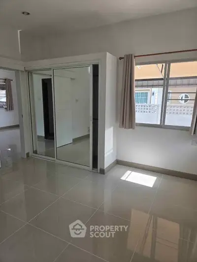 Spacious bedroom with mirrored closet and large window for natural light.
