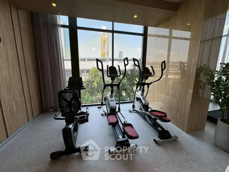 Modern gym with exercise bikes and scenic view of bridge through large windows.