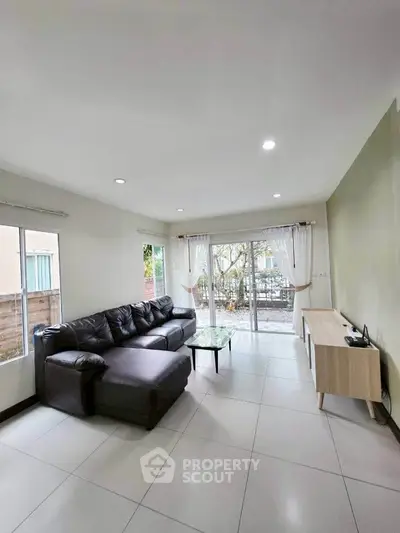 Spacious living room with modern furniture and large windows offering garden view.
