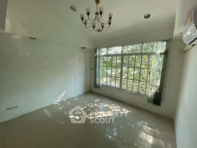 Spacious empty room with large window and chandelier, perfect for customization.