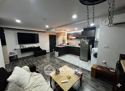 Modern open-layout living room with kitchen, featuring sleek appliances and cozy decor.