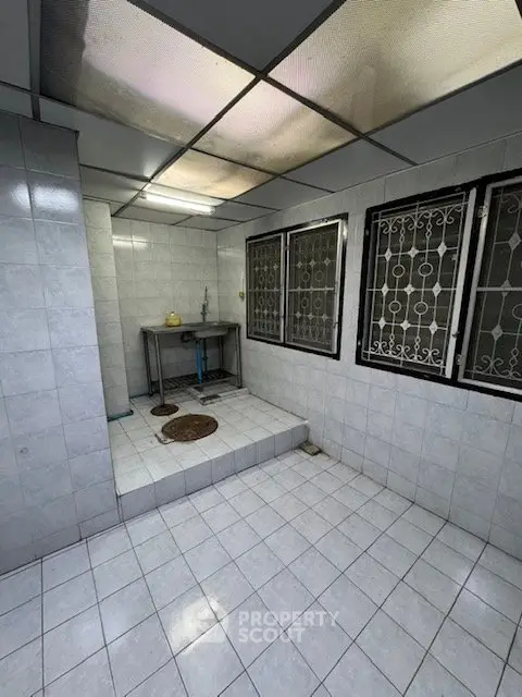 Spacious tiled room with metal sink and barred windows, ideal for utility or storage use.
