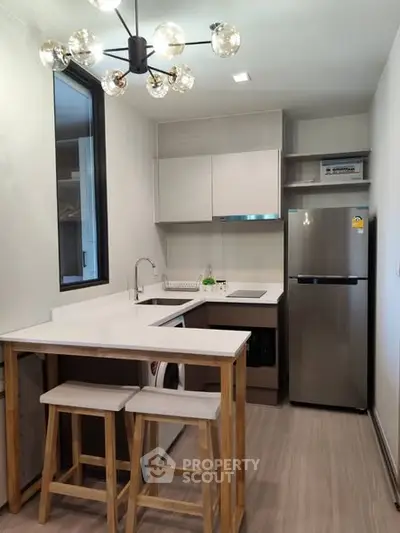 Modern kitchen with sleek design, featuring stainless steel fridge and stylish lighting.