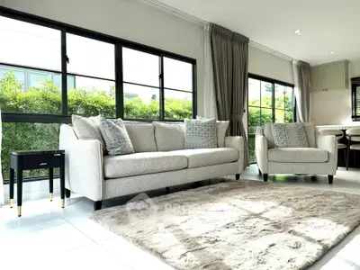 Spacious living room with modern sofa set and large windows offering lush garden views.
