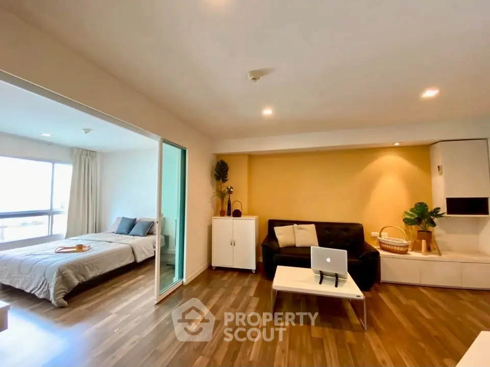 Modern living room with cozy seating and adjacent bedroom in open layout apartment.