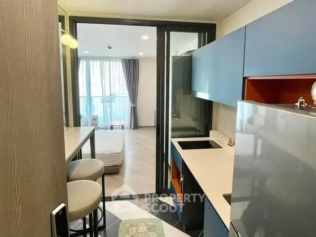 Modern compact kitchen with open layout leading to a bright living area with large windows.