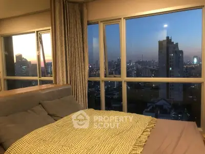 Luxurious bedroom with stunning city skyline view at sunset, featuring large windows and cozy bedding.