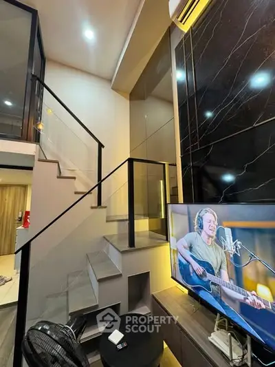 Modern duplex interior with sleek staircase and stylish living area featuring a large TV and contemporary decor.