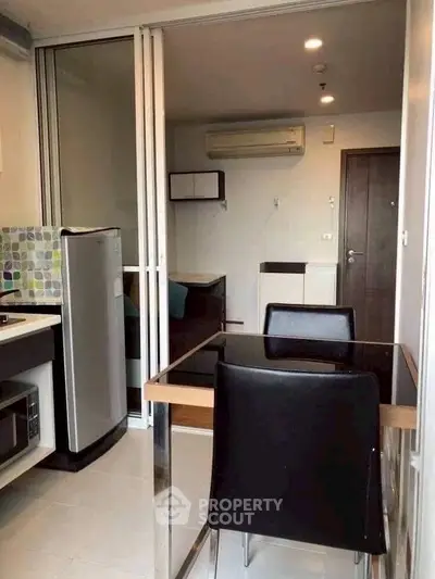 Modern apartment dining area with sleek black chairs and compact kitchen setup.