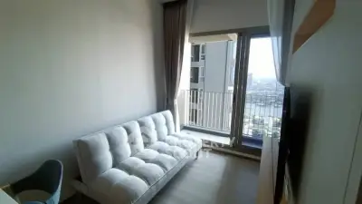 Modern living room with balcony and city view, featuring a stylish sofa and floor-to-ceiling windows.