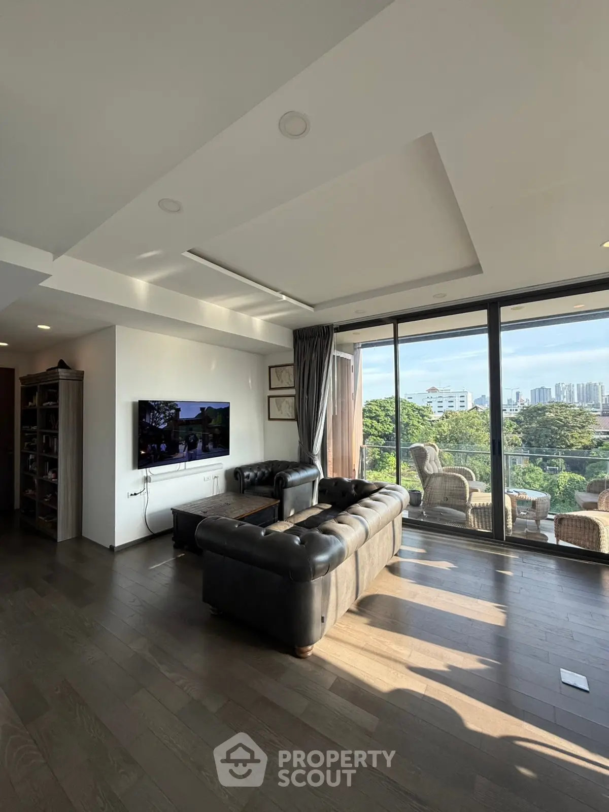 Spacious living room with large windows and city view, featuring elegant leather sofas and modern decor.