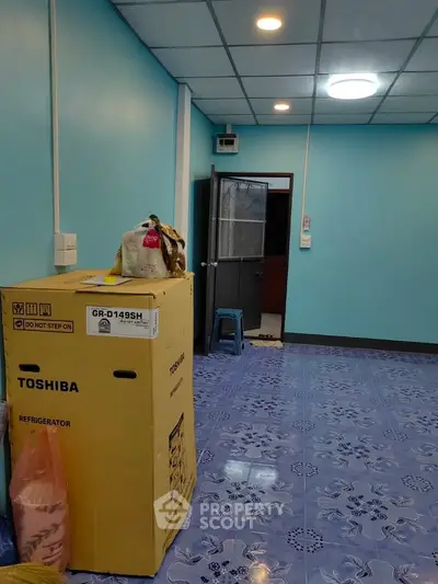 Spacious room with blue walls and tiled floor, featuring a new Toshiba refrigerator in packaging.