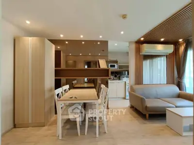Modern open-plan living room with dining area and kitchen, featuring sleek furniture and natural lighting.