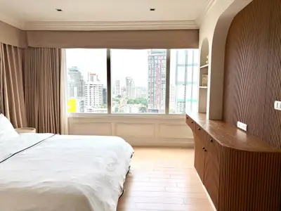 Spacious bedroom with large window offering stunning city views, featuring elegant built-in wooden cabinetry.