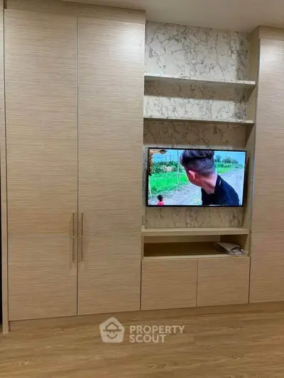 Modern living room with built-in wooden cabinets and a TV, featuring elegant marble accents.