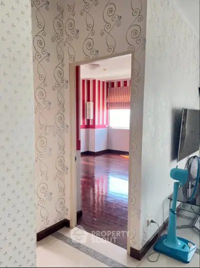 Stylish interior with patterned wallpaper and wooden flooring, featuring a glimpse into a vibrant room with natural light.