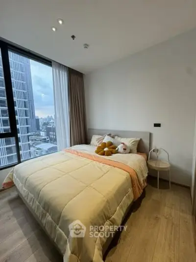 Modern bedroom with city view, featuring cozy bedding and large window for natural light.