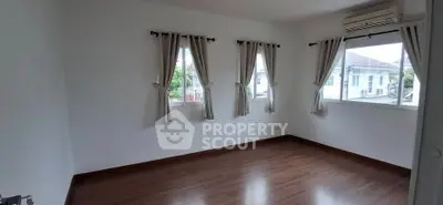 Spacious empty room with wooden flooring and large windows in a modern home.