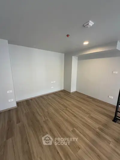 Spacious empty room with wooden flooring and modern lighting, perfect for customization.