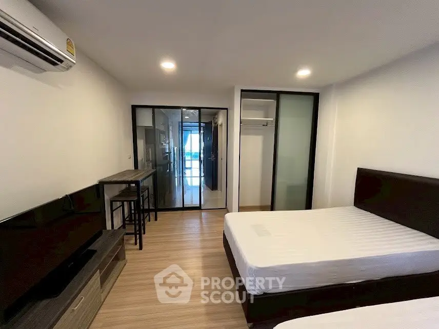 Modern bedroom with twin beds, sleek furniture, and glass sliding doors leading to a bright living area.