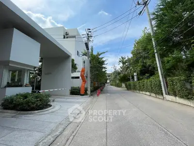 Modern residential building entrance with lush greenery and clear blue sky.