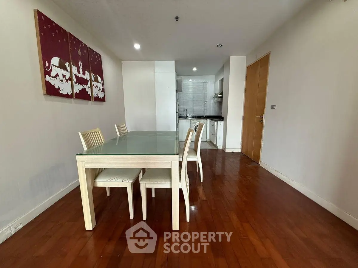 Modern dining area with glass table and wooden flooring in open layout apartment.