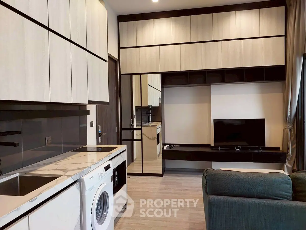 Modern living room with sleek cabinetry, washing machine, and flat-screen TV in stylish apartment.