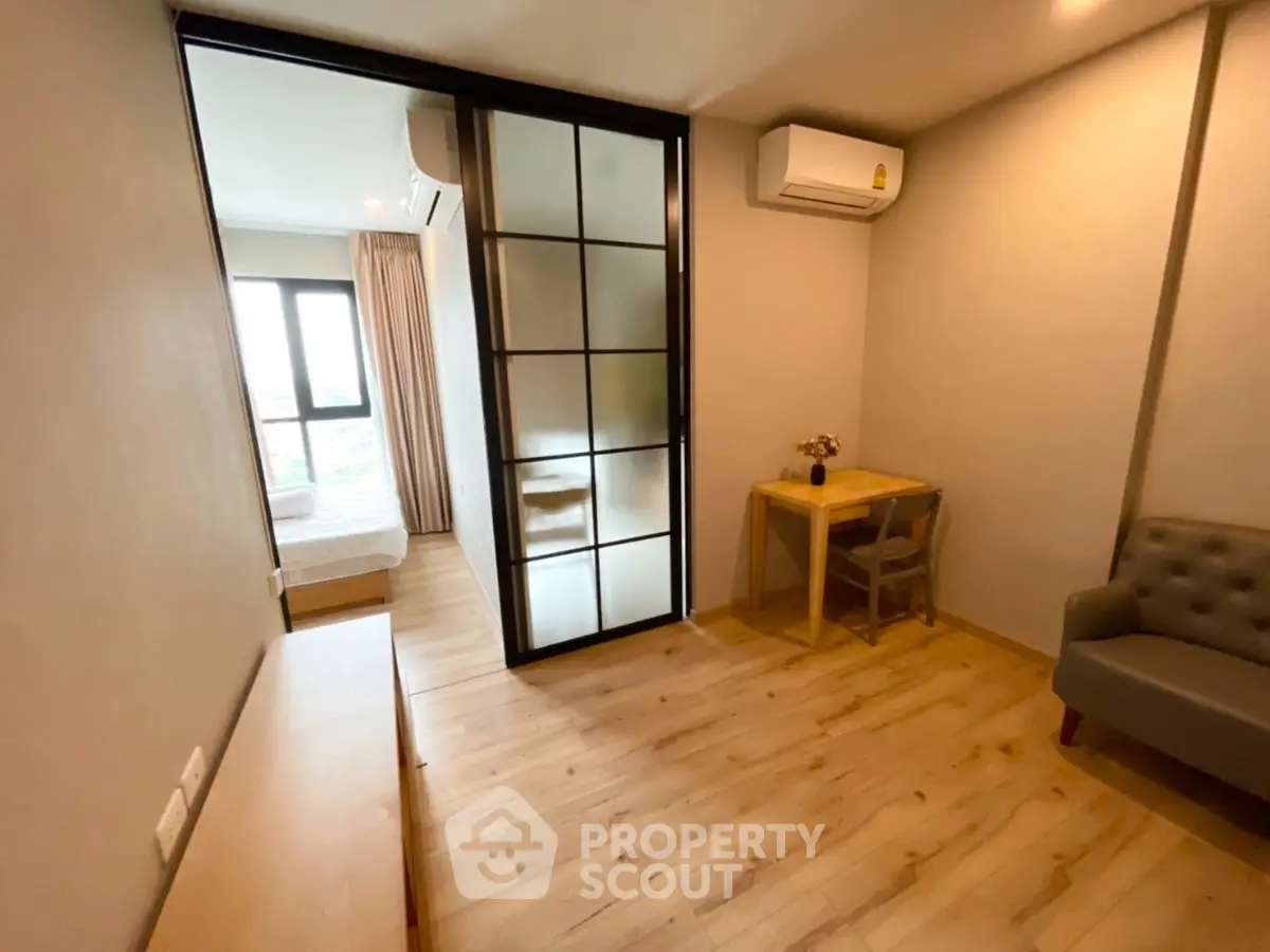 Modern apartment interior with cozy living area and bedroom separated by glass partition.