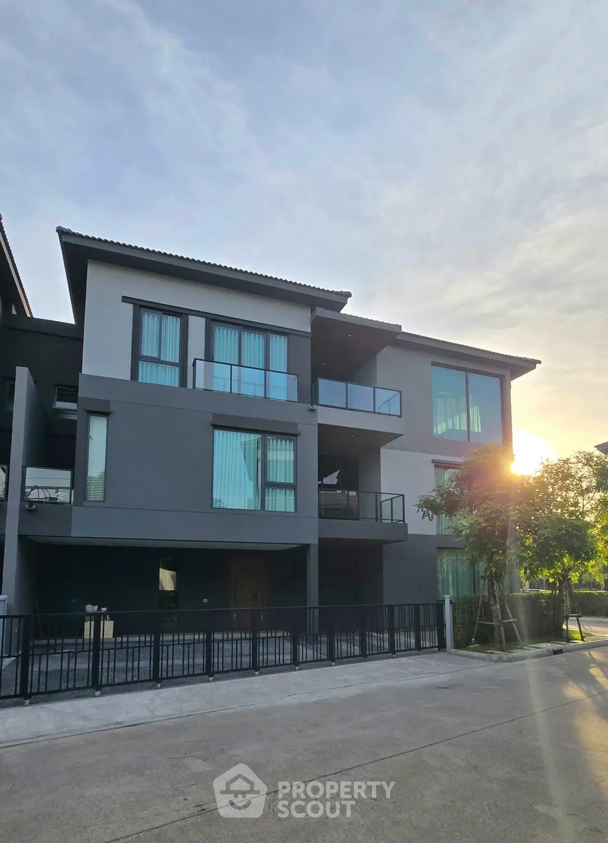 Modern three-story building with large windows and balconies at sunset.