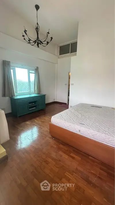 Spacious bedroom with wooden flooring and large window offering natural light.