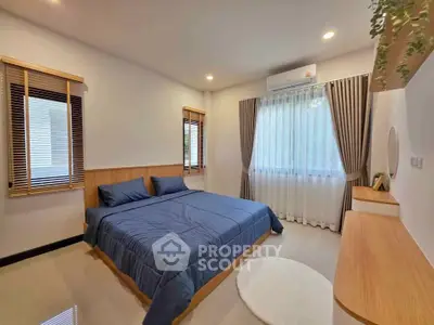 Modern bedroom with blue bedding and natural wood accents, featuring large windows and stylish curtains.