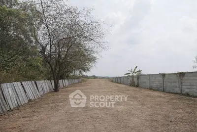 Expansive vacant land with potential for development, bordered by trees and fences, under a clear sky.