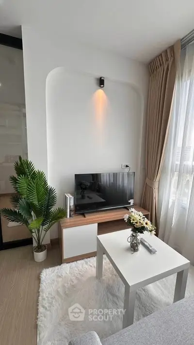 Modern living room with stylish decor, TV setup, and natural light from large windows.