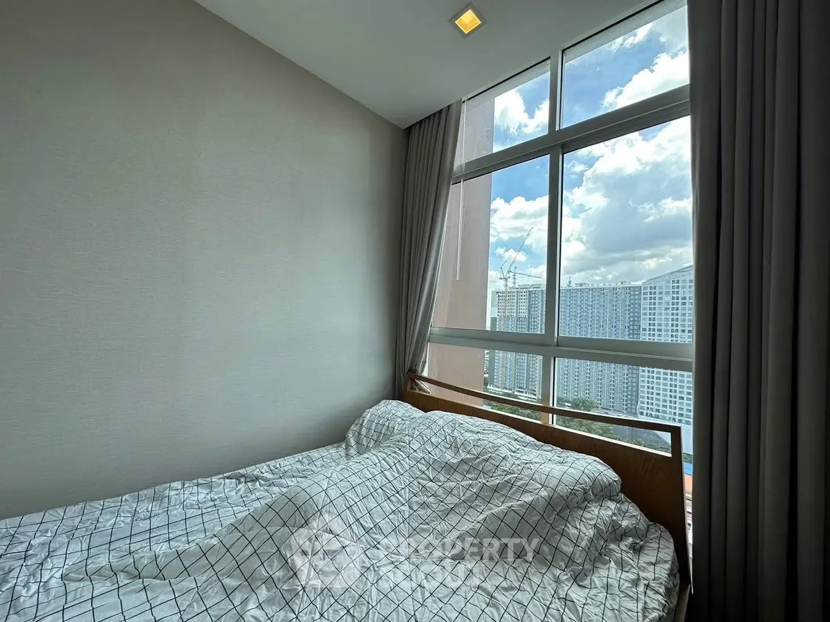 Cozy bedroom with large window offering stunning city view, perfect for urban living.