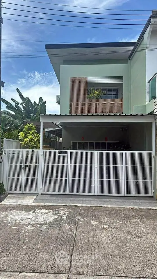 Modern two-story house with gated entrance and lush greenery, perfect for family living.