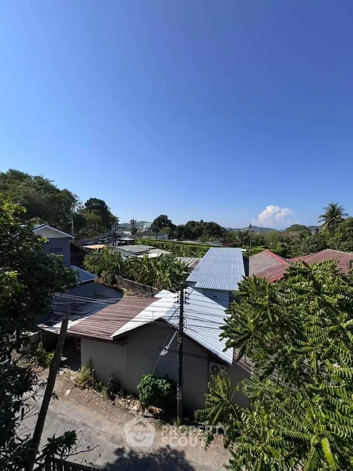 Scenic view of residential rooftops surrounded by lush greenery under a clear blue sky.